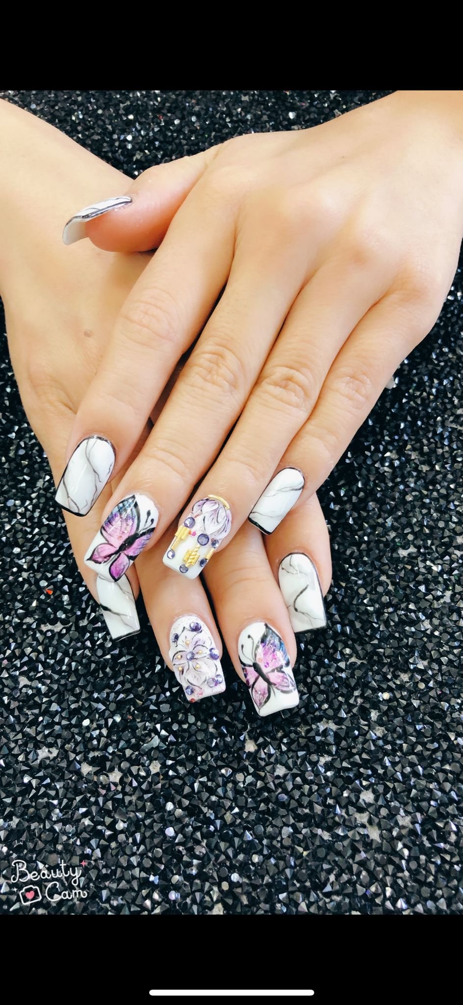 Elegant white marble nails with hand-painted purple butterflies, floral accents, and crystal embellishments – Moon Nail Spa Singapore.
